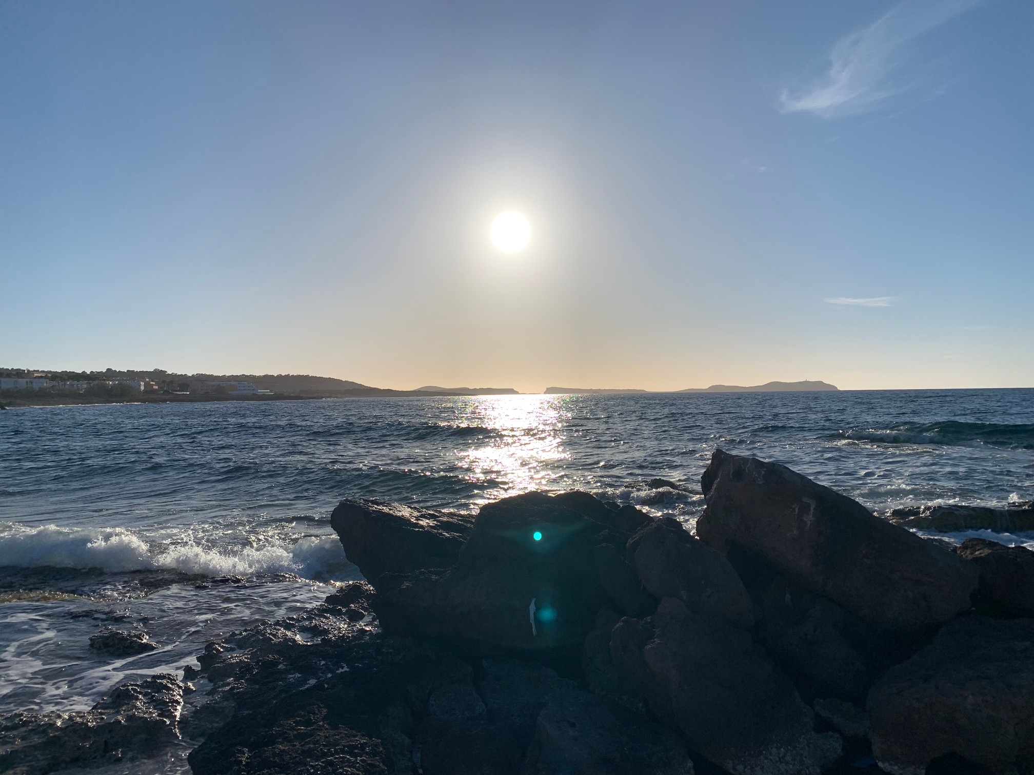 Vue sur la mer, avec des rochers au premier plan. La mer est légèrement agitée. On voit des collines au loin.